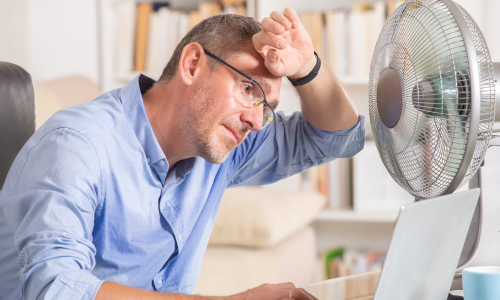 Imagem ilustrativa de homem passando calor com ventilador ligado.